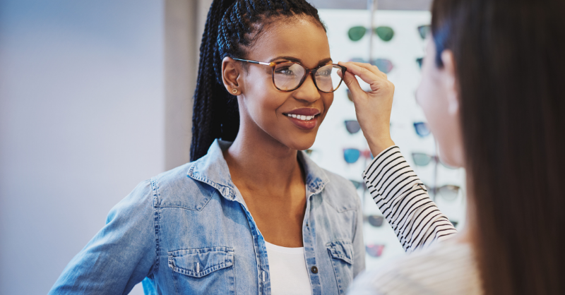 An optician helping a patient try on glasses at the office.