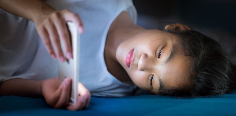 A woman lying in bed on her side, playing on her phone.