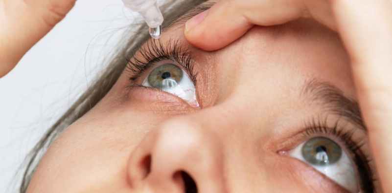 A woman inserting eye drops into her right eye.