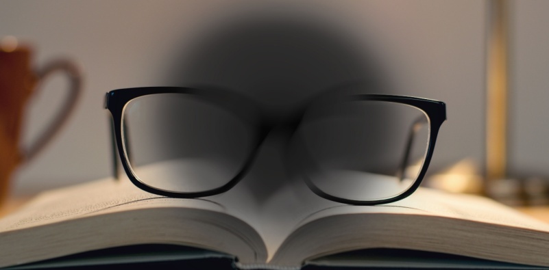 A visual representation of age-related macular degeneration, showing central vision loss looking at a book with a pair of glasses sat on the top.